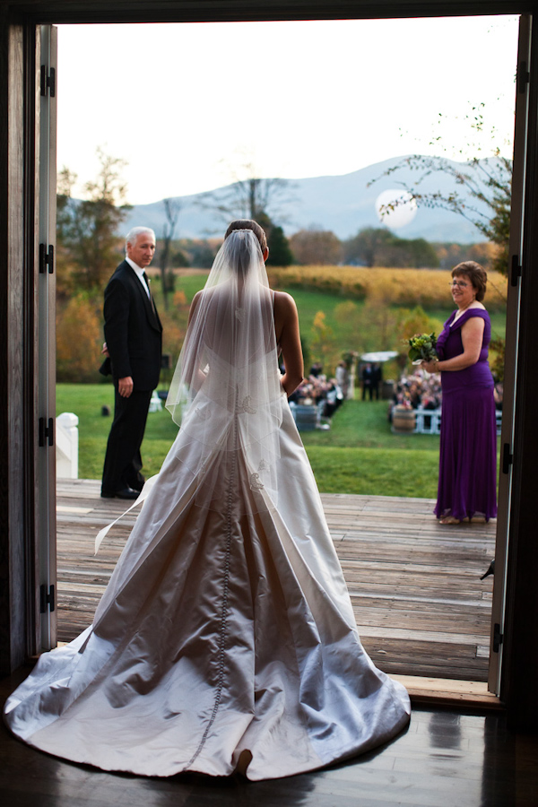 beautiful image of the bride standing under doorway entering the outside ceremony - bride is wearing full length veil and ball gown style dress - photo by Washington DC based wedding photographers Holland Photo Arts